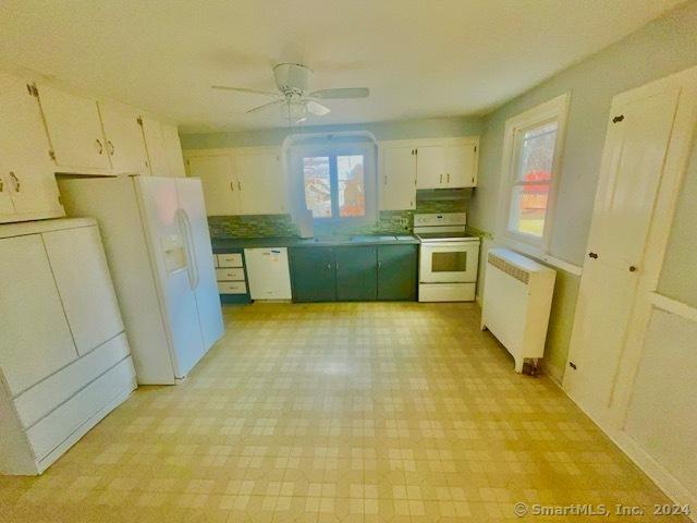 kitchen featuring white appliances, ceiling fan, radiator heating unit, white cabinetry, and washer / dryer