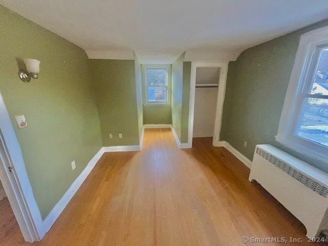 unfurnished bedroom featuring radiator, lofted ceiling, light hardwood / wood-style flooring, and multiple windows