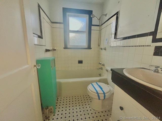 full bathroom with vanity, tiled shower / bath combo, tile walls, and toilet