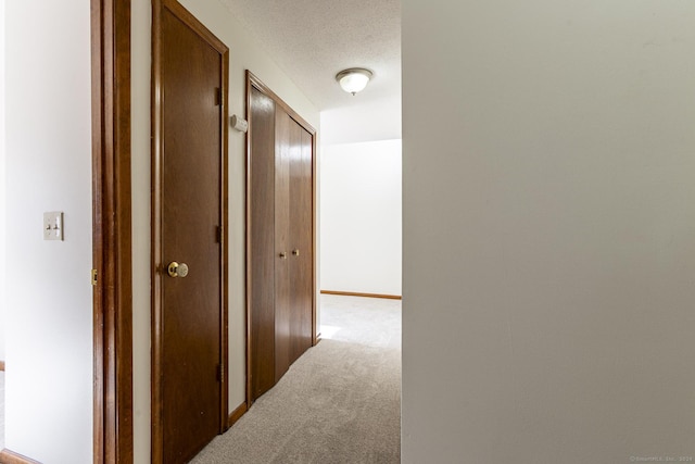 hall with light colored carpet and a textured ceiling