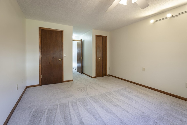 empty room with ceiling fan, light colored carpet, and a textured ceiling