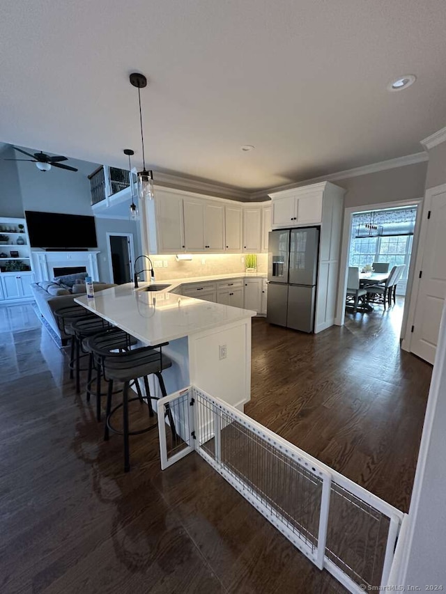 kitchen featuring kitchen peninsula, stainless steel fridge, sink, white cabinets, and a breakfast bar area