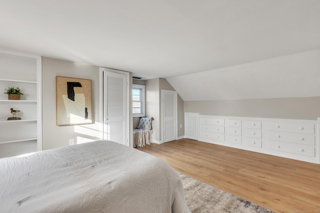 bedroom featuring two closets, light wood-type flooring, and vaulted ceiling