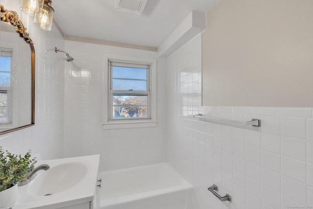 bathroom with vanity, tile walls, and tiled shower / bath