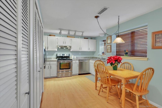 kitchen with white cabinetry, stainless steel appliances, hanging light fixtures, and light hardwood / wood-style flooring