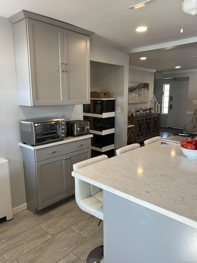 kitchen featuring a toaster, baseboards, light stone counters, gray cabinetry, and recessed lighting