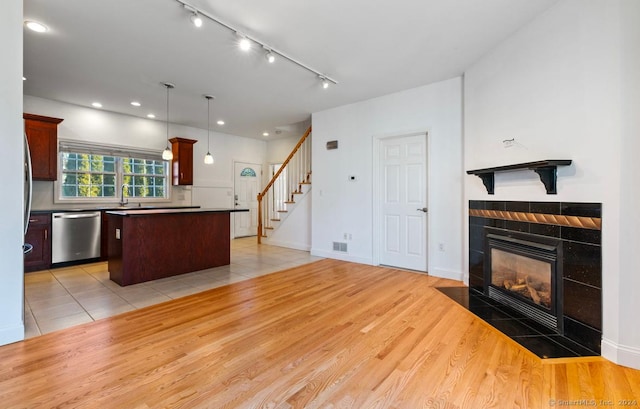 kitchen with pendant lighting, a center island, light hardwood / wood-style flooring, stainless steel dishwasher, and a fireplace