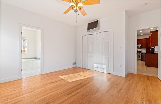 unfurnished bedroom featuring ensuite bathroom, sink, ceiling fan, light wood-type flooring, and a closet