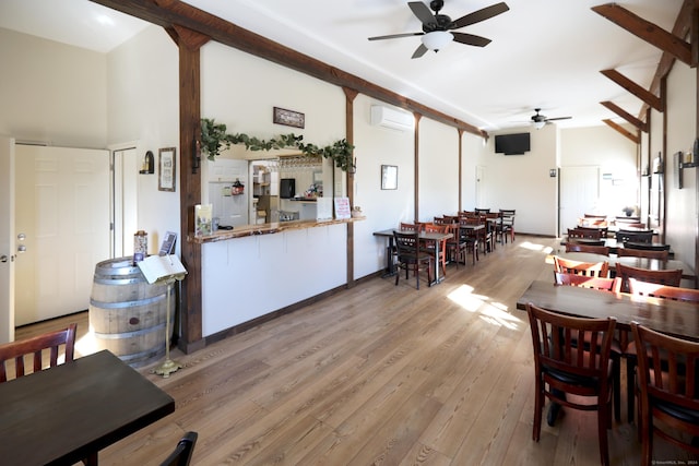 dining space featuring ceiling fan, light hardwood / wood-style floors, an AC wall unit, and a high ceiling