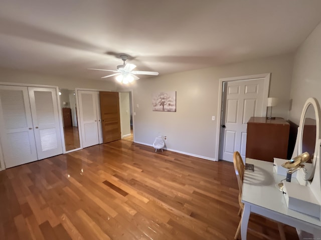 unfurnished bedroom with ceiling fan, wood-type flooring, and two closets