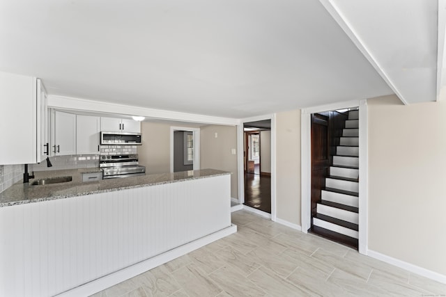 kitchen with light stone countertops, appliances with stainless steel finishes, white cabinets, and kitchen peninsula