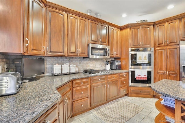 kitchen featuring backsplash, stainless steel appliances, light stone counters, and light tile patterned flooring