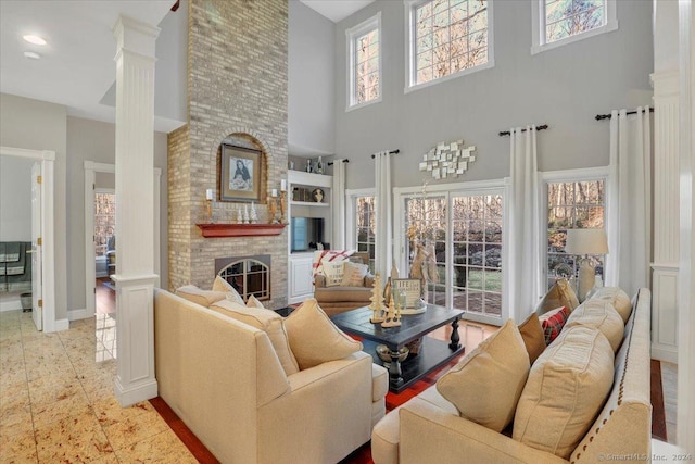 living room featuring a brick fireplace, a towering ceiling, and decorative columns