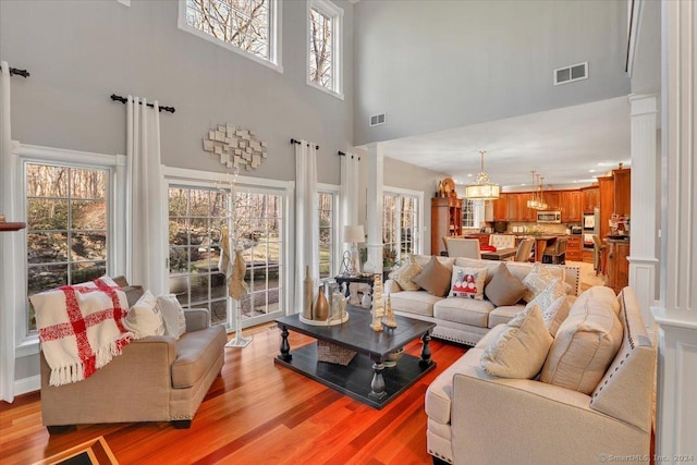 living room with a notable chandelier, light hardwood / wood-style floors, a towering ceiling, and decorative columns