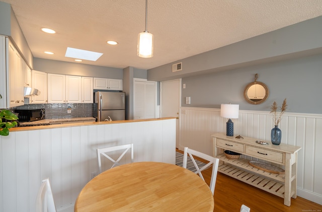 kitchen with kitchen peninsula, a skylight, pendant lighting, wood-type flooring, and stainless steel refrigerator