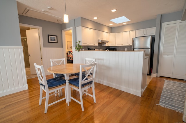 dining area featuring a skylight, light hardwood / wood-style floors, and a textured ceiling