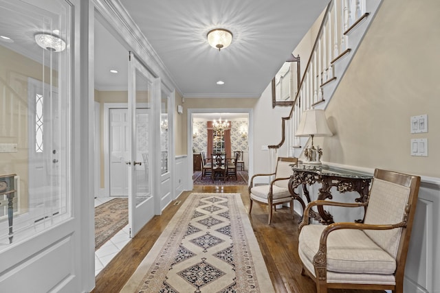 hallway with wood-type flooring, ornamental molding, french doors, and an inviting chandelier