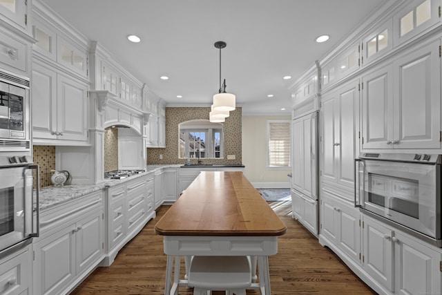 kitchen featuring wood counters, decorative backsplash, stainless steel appliances, a center island, and white cabinetry