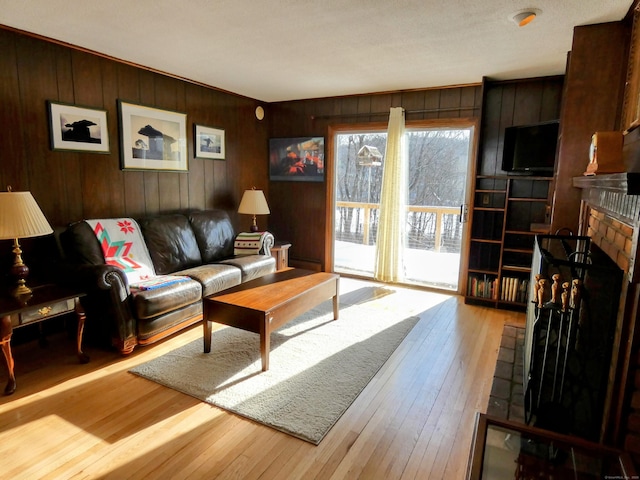 living room with a brick fireplace, light wood-type flooring, and wood walls