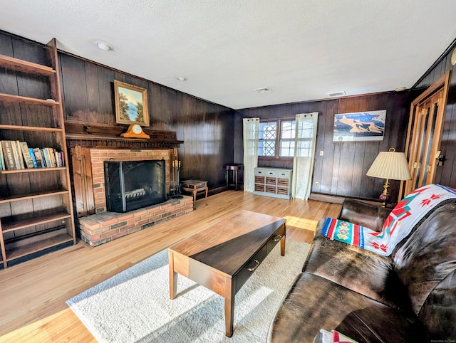 living room with wooden walls, a fireplace, light hardwood / wood-style flooring, and a textured ceiling