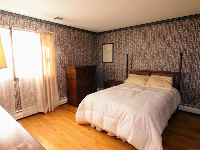 bedroom with hardwood / wood-style flooring, a baseboard radiator, and a textured ceiling