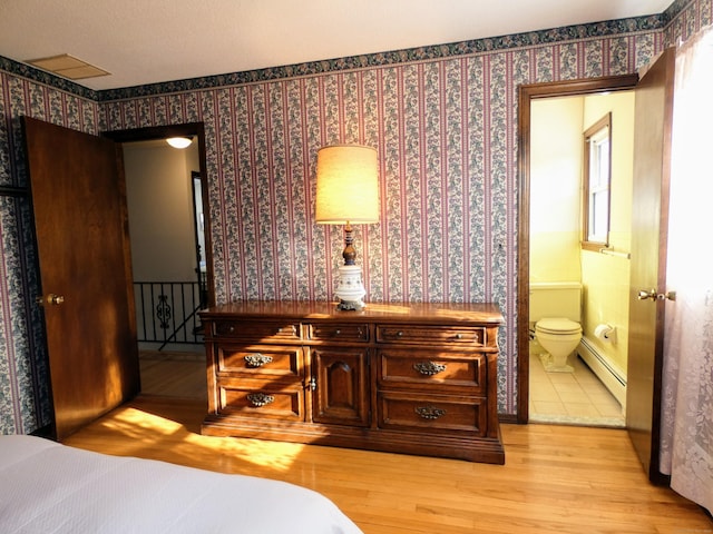 bedroom featuring a baseboard radiator, ensuite bathroom, and light hardwood / wood-style flooring