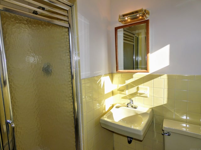 bathroom with a shower with shower door, sink, tile walls, and toilet