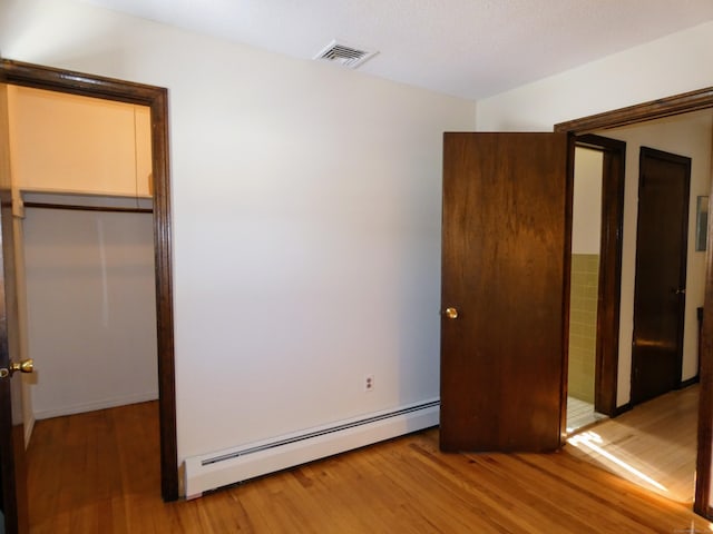 unfurnished bedroom with hardwood / wood-style flooring, a baseboard radiator, and a closet