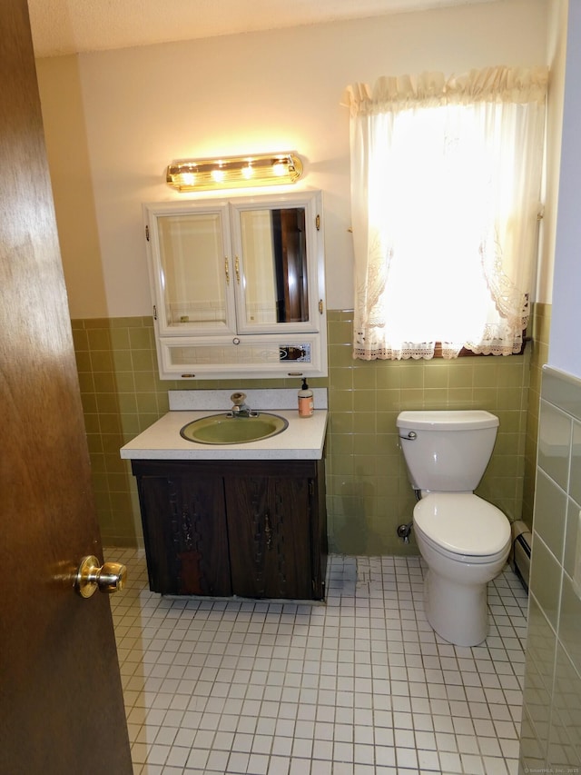 bathroom with tile walls, vanity, a baseboard heating unit, toilet, and tile patterned floors