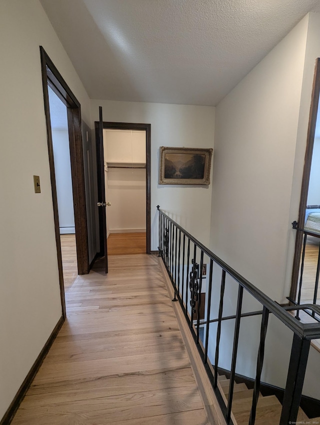 corridor with a textured ceiling and light hardwood / wood-style floors