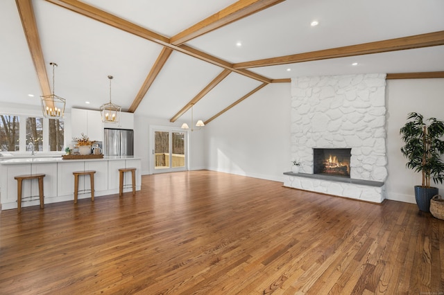 living room featuring hardwood / wood-style flooring, vaulted ceiling with beams, a stone fireplace, and sink