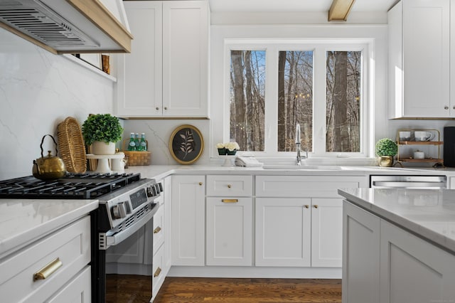 kitchen featuring custom exhaust hood, stainless steel gas range oven, sink, tasteful backsplash, and white cabinetry