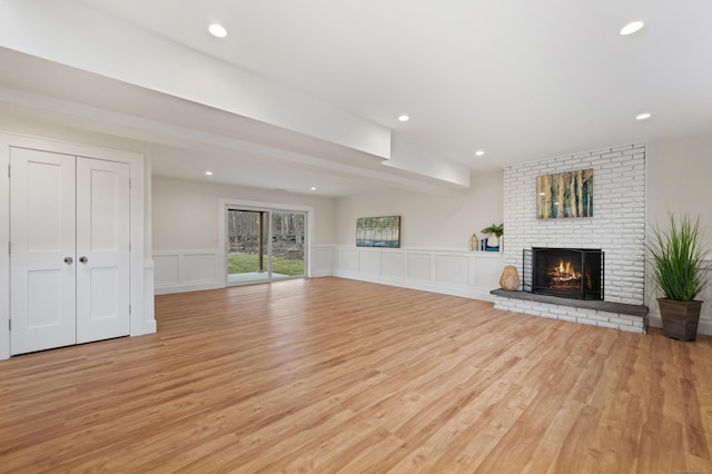 unfurnished living room with a fireplace, beam ceiling, and light wood-type flooring