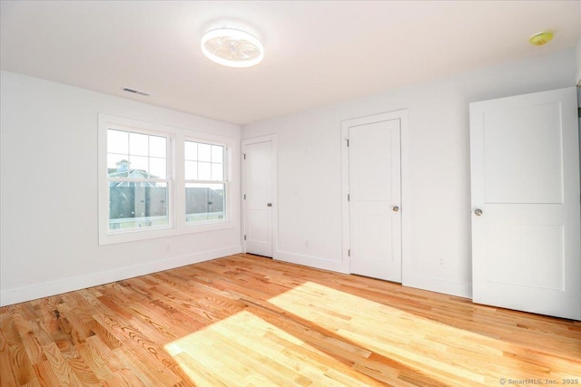 unfurnished bedroom with light hardwood / wood-style floors and multiple closets