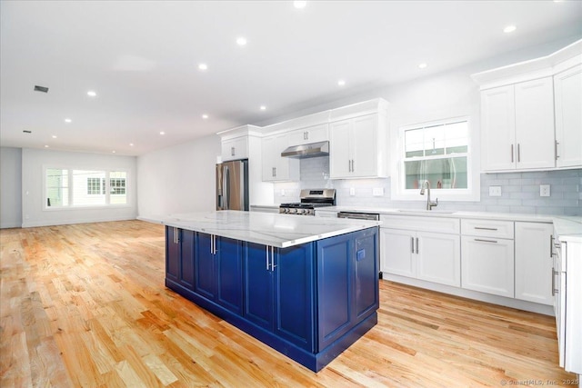 kitchen featuring appliances with stainless steel finishes, white cabinetry, sink, a center island, and light stone counters