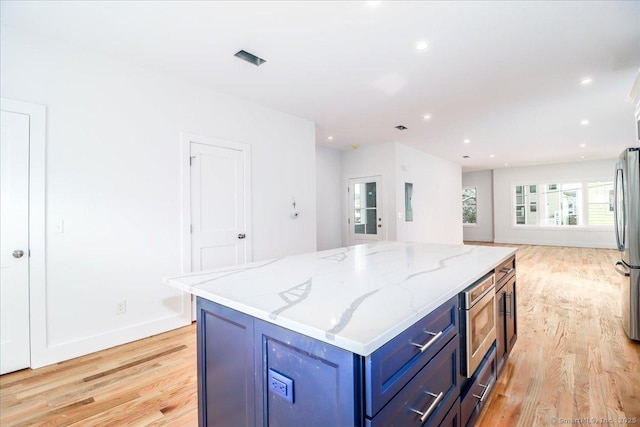 kitchen with blue cabinetry, appliances with stainless steel finishes, a center island, light stone counters, and light wood-type flooring