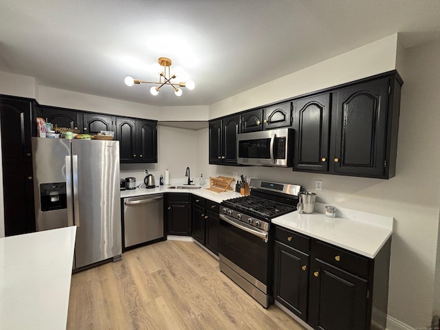 kitchen with sink, stainless steel appliances, light wood-type flooring, and a notable chandelier