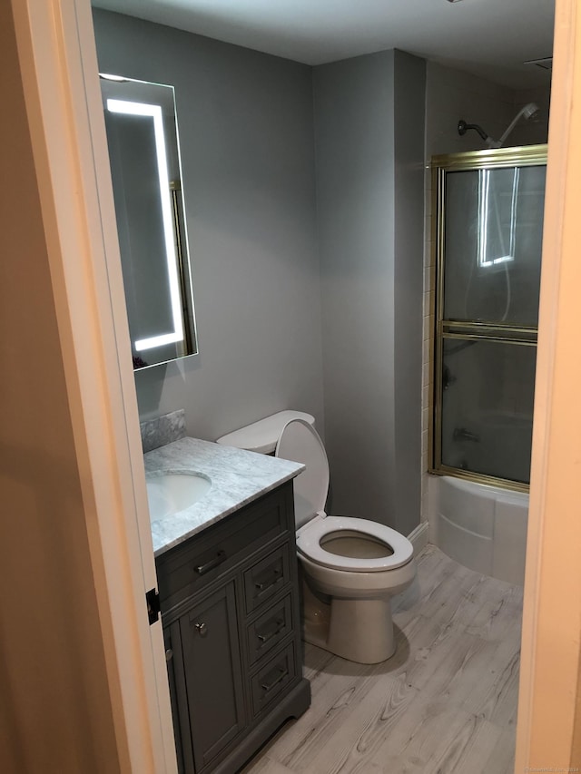 full bathroom featuring hardwood / wood-style floors, vanity, toilet, and enclosed tub / shower combo