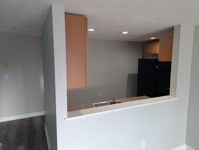 kitchen with kitchen peninsula, black refrigerator, dark wood-type flooring, and sink