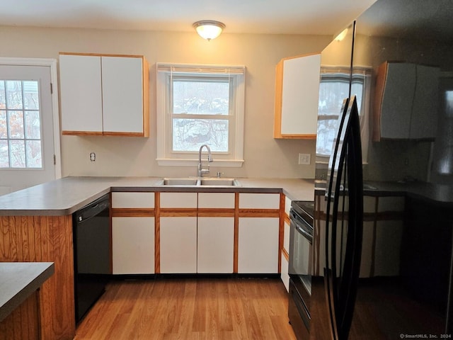 kitchen with kitchen peninsula, light wood-type flooring, black appliances, sink, and white cabinetry