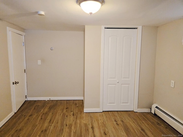 unfurnished bedroom with wood-type flooring, a baseboard radiator, and a closet