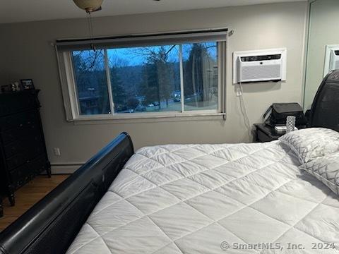 bedroom featuring hardwood / wood-style flooring, an AC wall unit, and baseboard heating