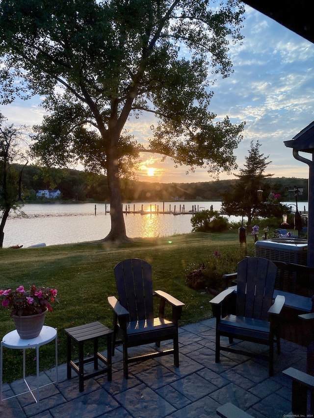 patio terrace at dusk featuring a lawn and a water view