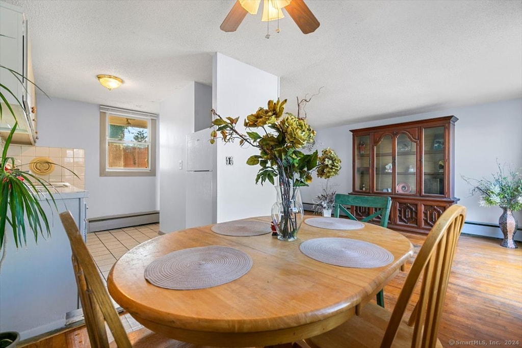 dining room with a textured ceiling, a baseboard radiator, light hardwood / wood-style flooring, and ceiling fan