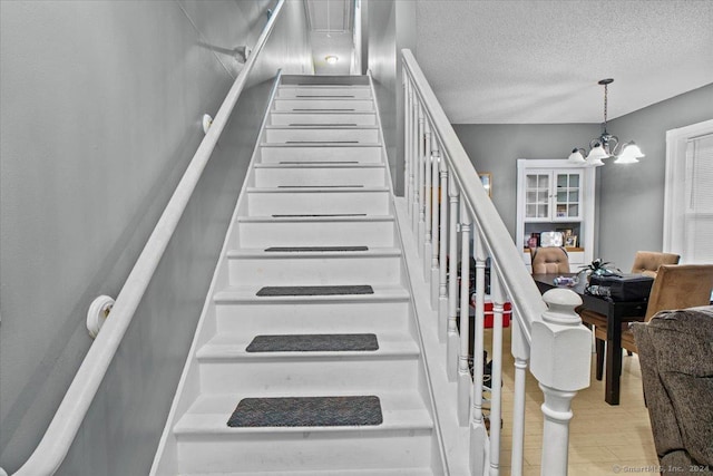 staircase featuring hardwood / wood-style floors, a chandelier, and a textured ceiling