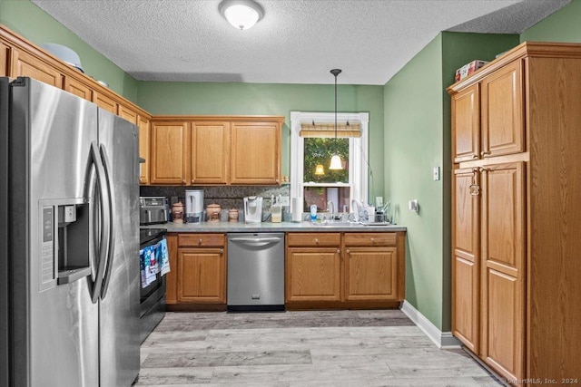 kitchen with tasteful backsplash, a textured ceiling, stainless steel appliances, pendant lighting, and light hardwood / wood-style flooring