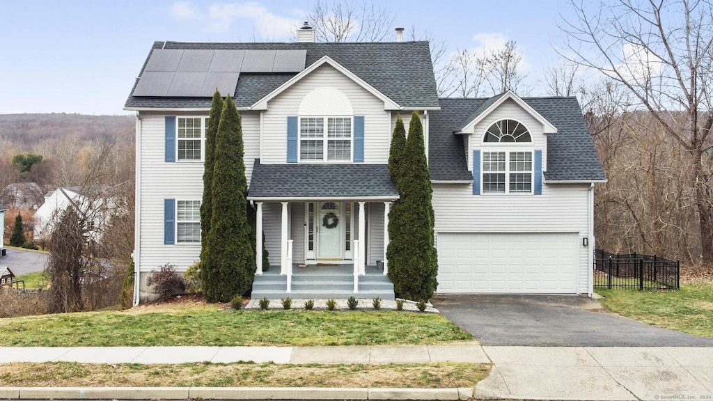 view of front of property with a front yard, solar panels, a garage, and a porch