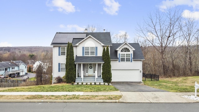 front of property featuring solar panels, covered porch, a front yard, and a garage