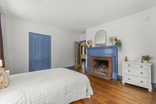 bedroom with dark hardwood / wood-style floors and a brick fireplace