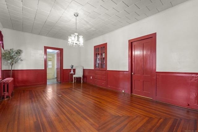 empty room with dark hardwood / wood-style flooring, radiator heating unit, ornamental molding, and an inviting chandelier